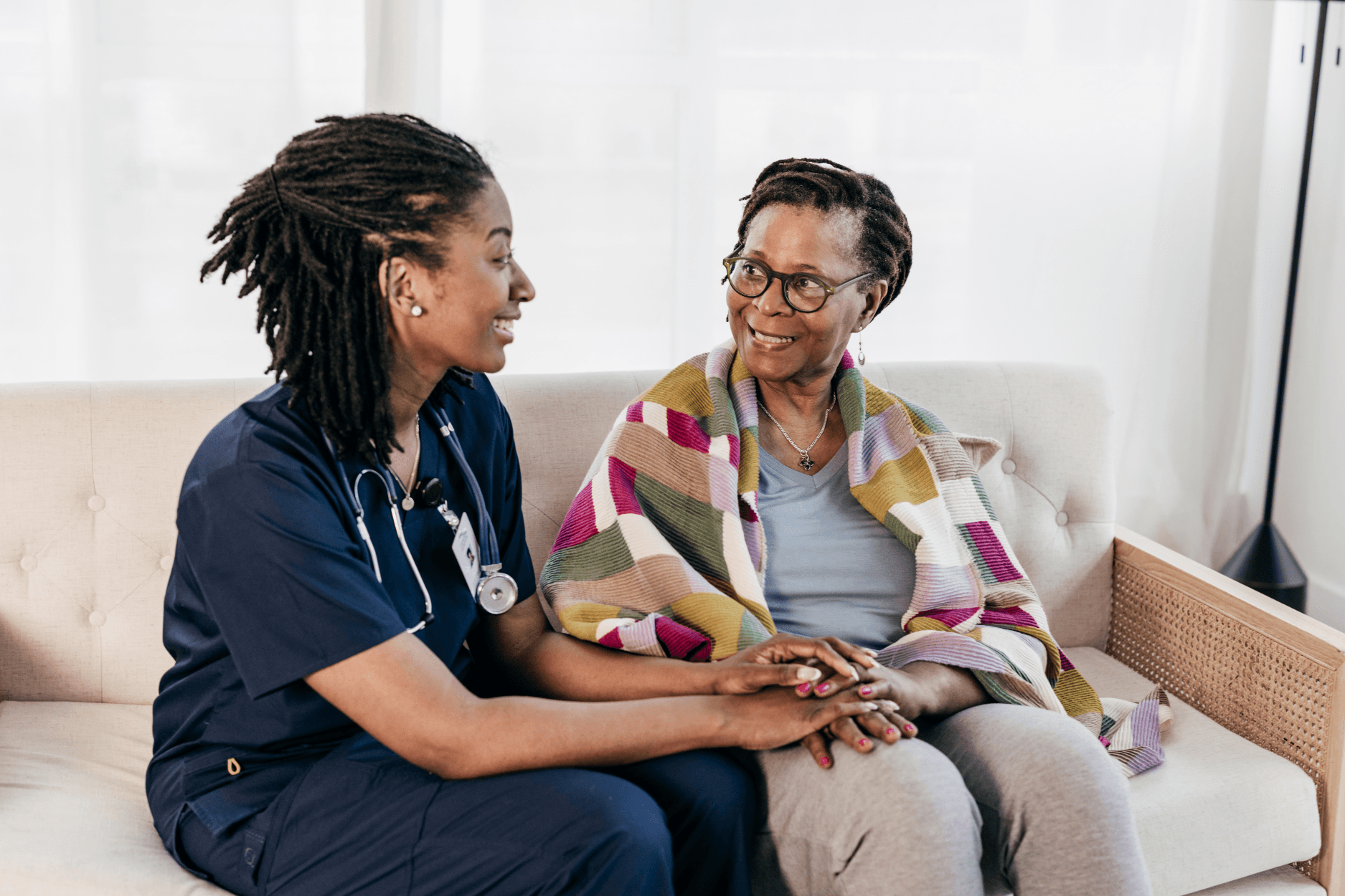A compassionate nurse holding hands with an elderly client on a sofa at home